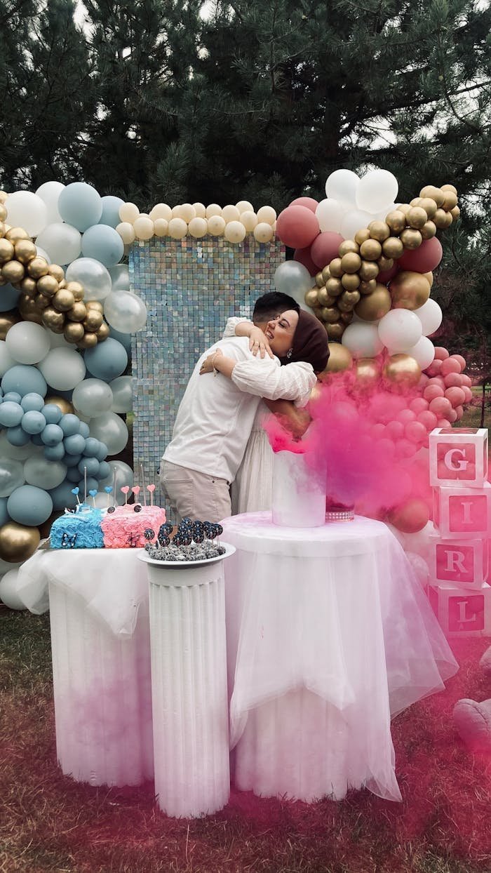 portfolio-01 Outdoor gender reveal party with balloons and cake, featuring a couple embracing joyfully.