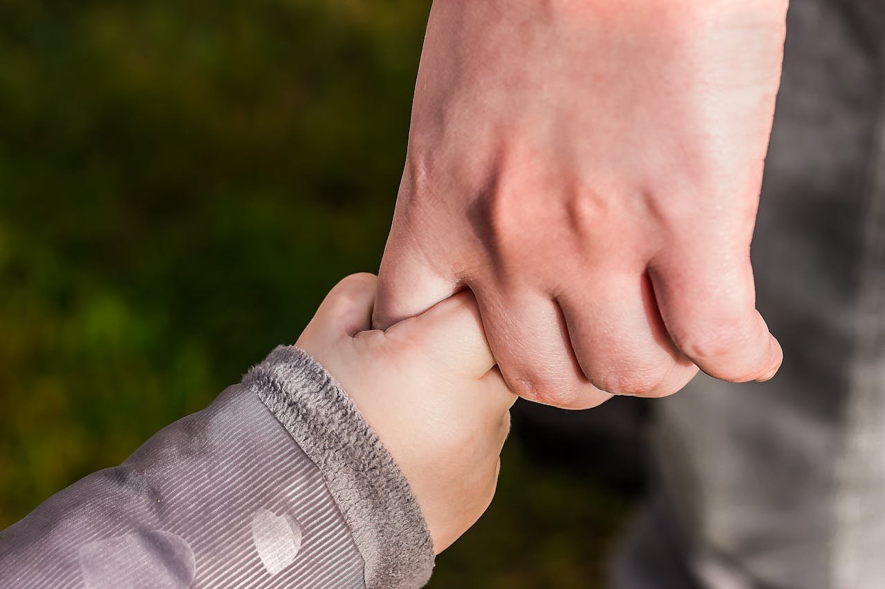 about-img A close-up of a child and parent holding hands in a park, symbolizing love and trust.